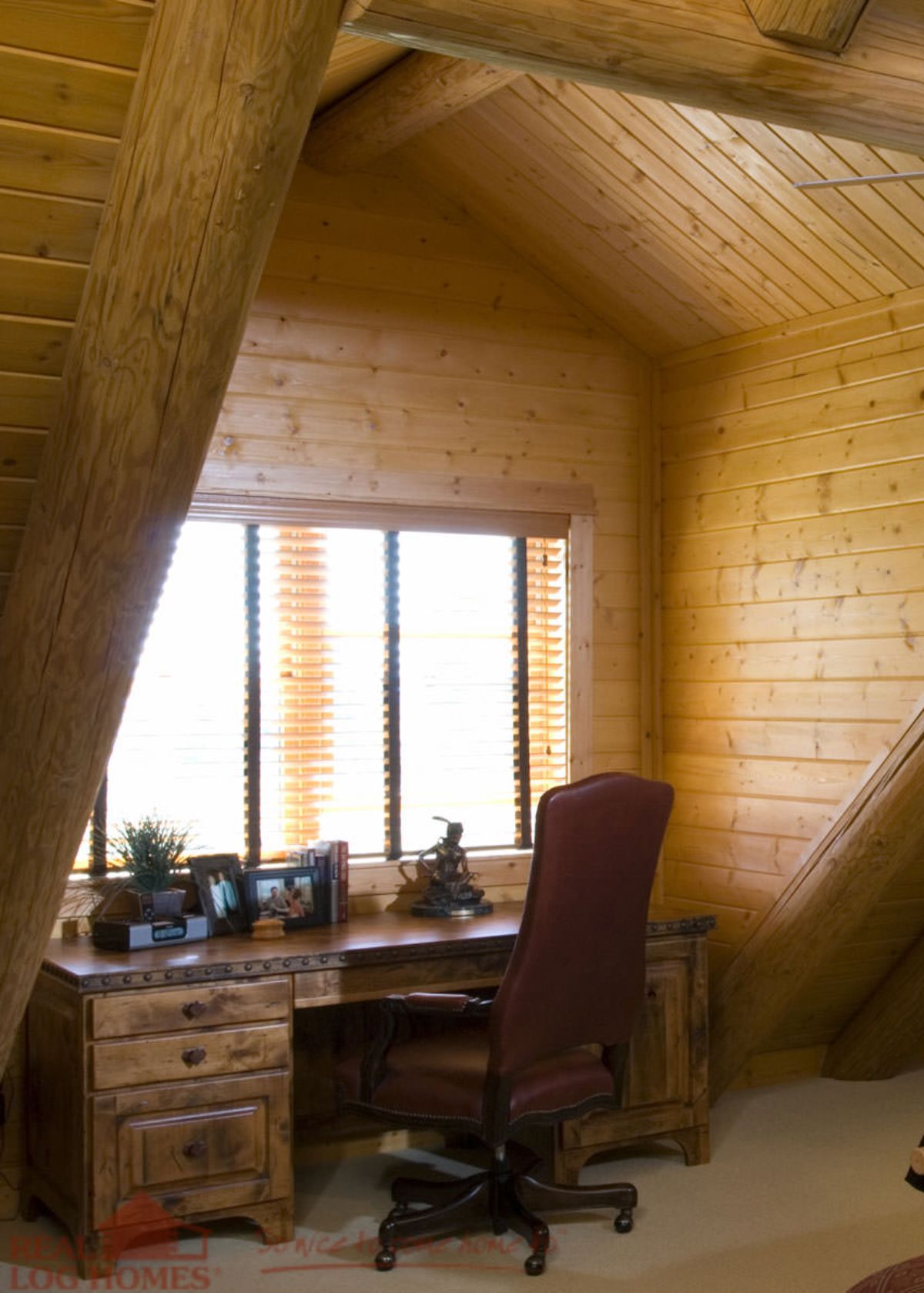 desk with maroon office chair under dormer window in log cabin