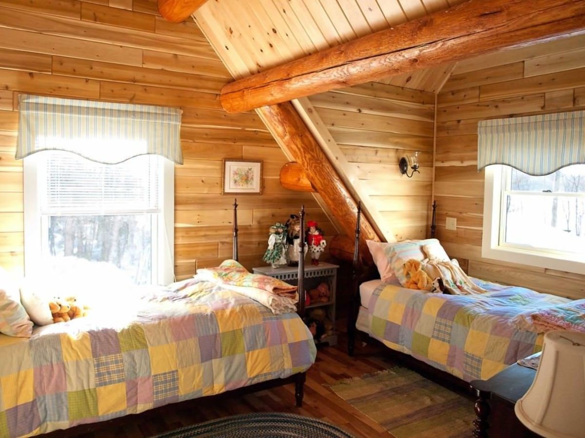light color block bedding on twin beds under loft roof in cabin with dormer window to right