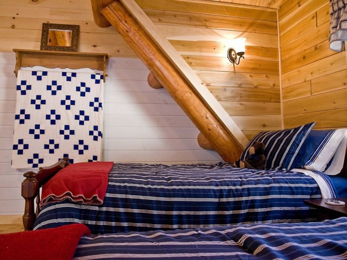 blue and whit striped bedding with red accents on twin beds under eaves in log cabin
