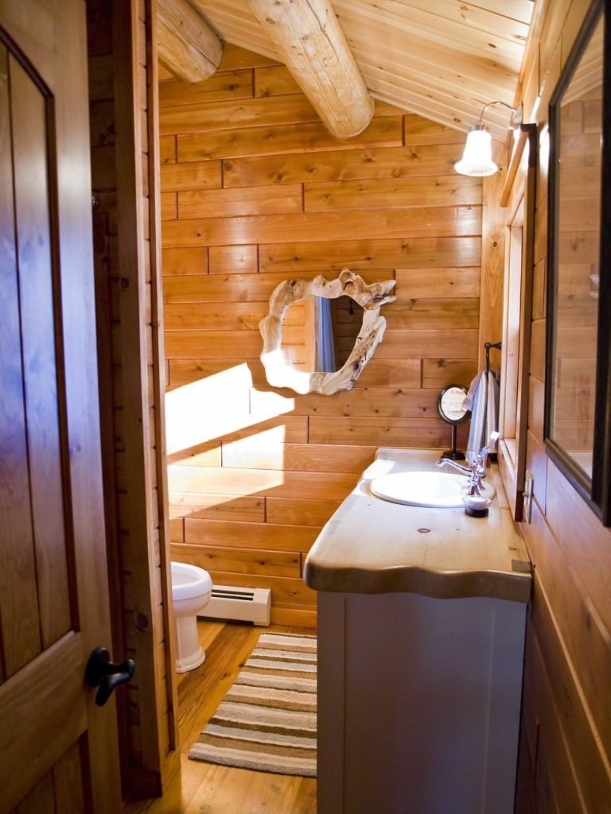 view into bathroom with light wood vanity and round mirror against back wall