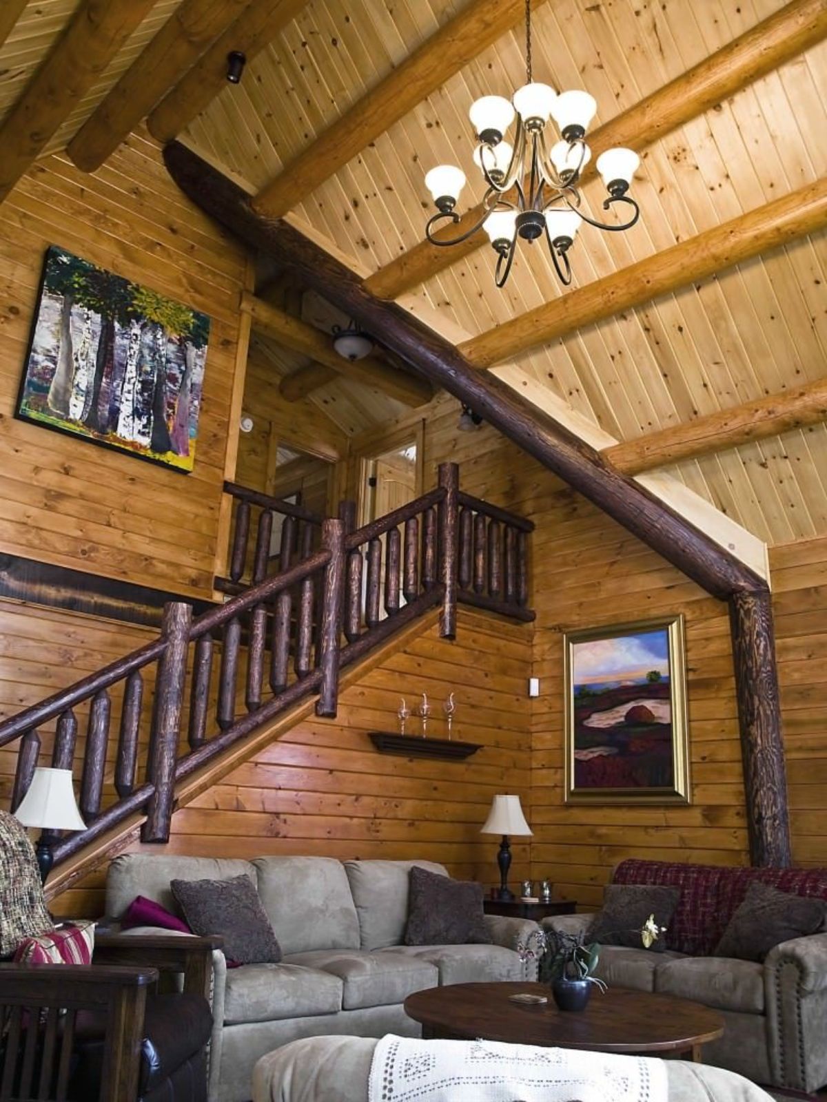 gray sofa against stairs in log cabin with chandelier on log cabin ceiling