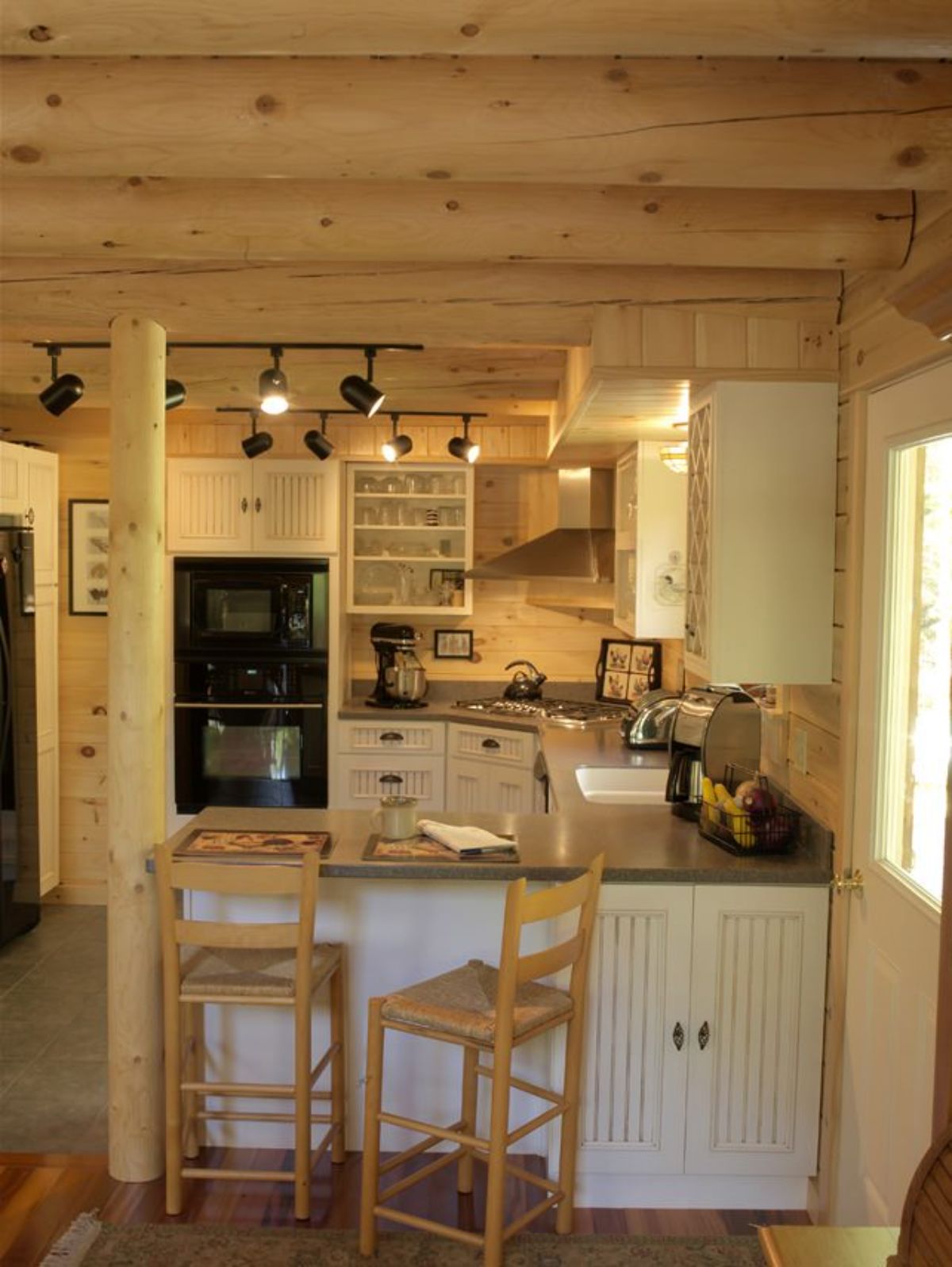 view into kitchen with light wood cabinets and stools in foreground