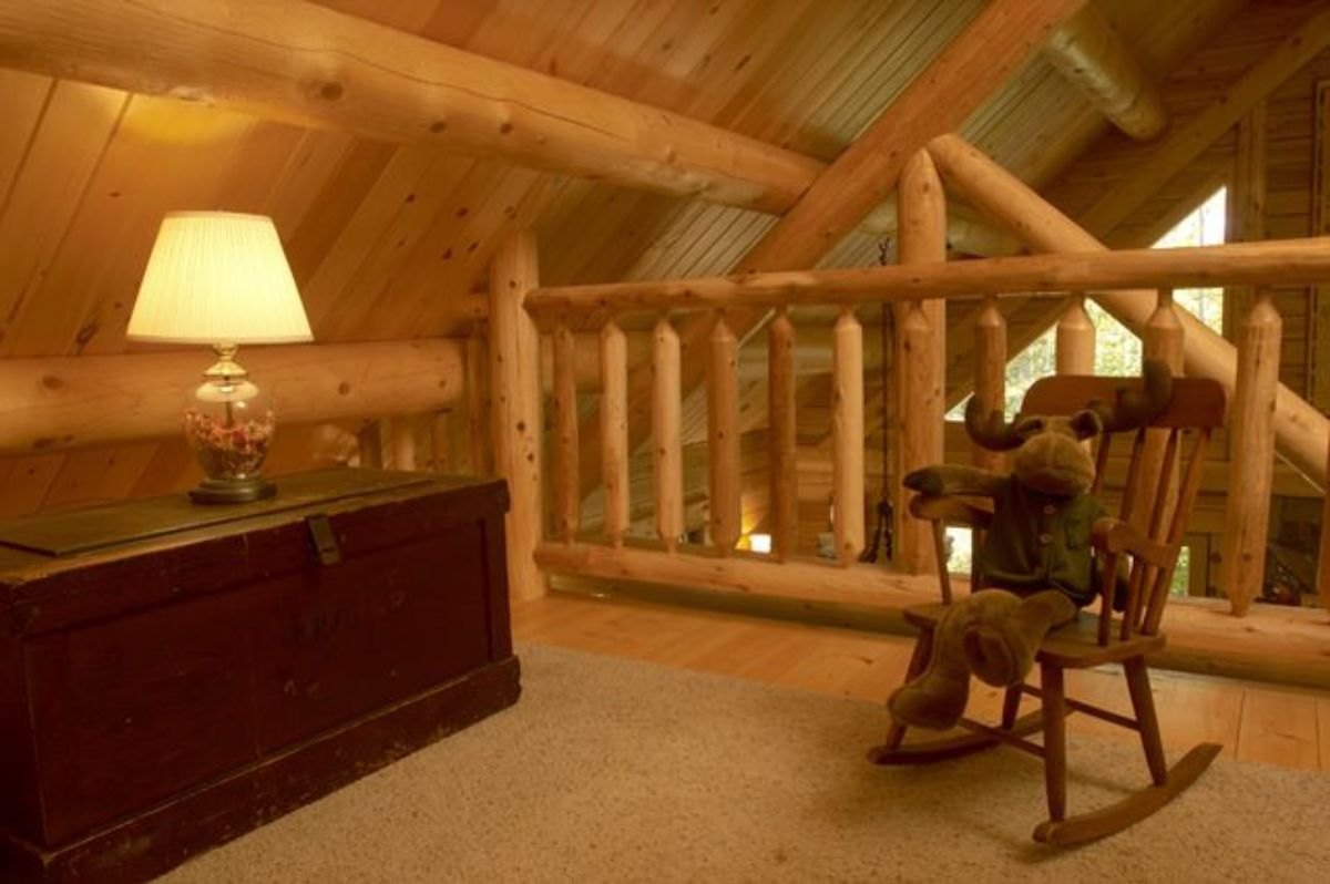 loft with rocking chair on right and dark wood chest with lamp on top on left