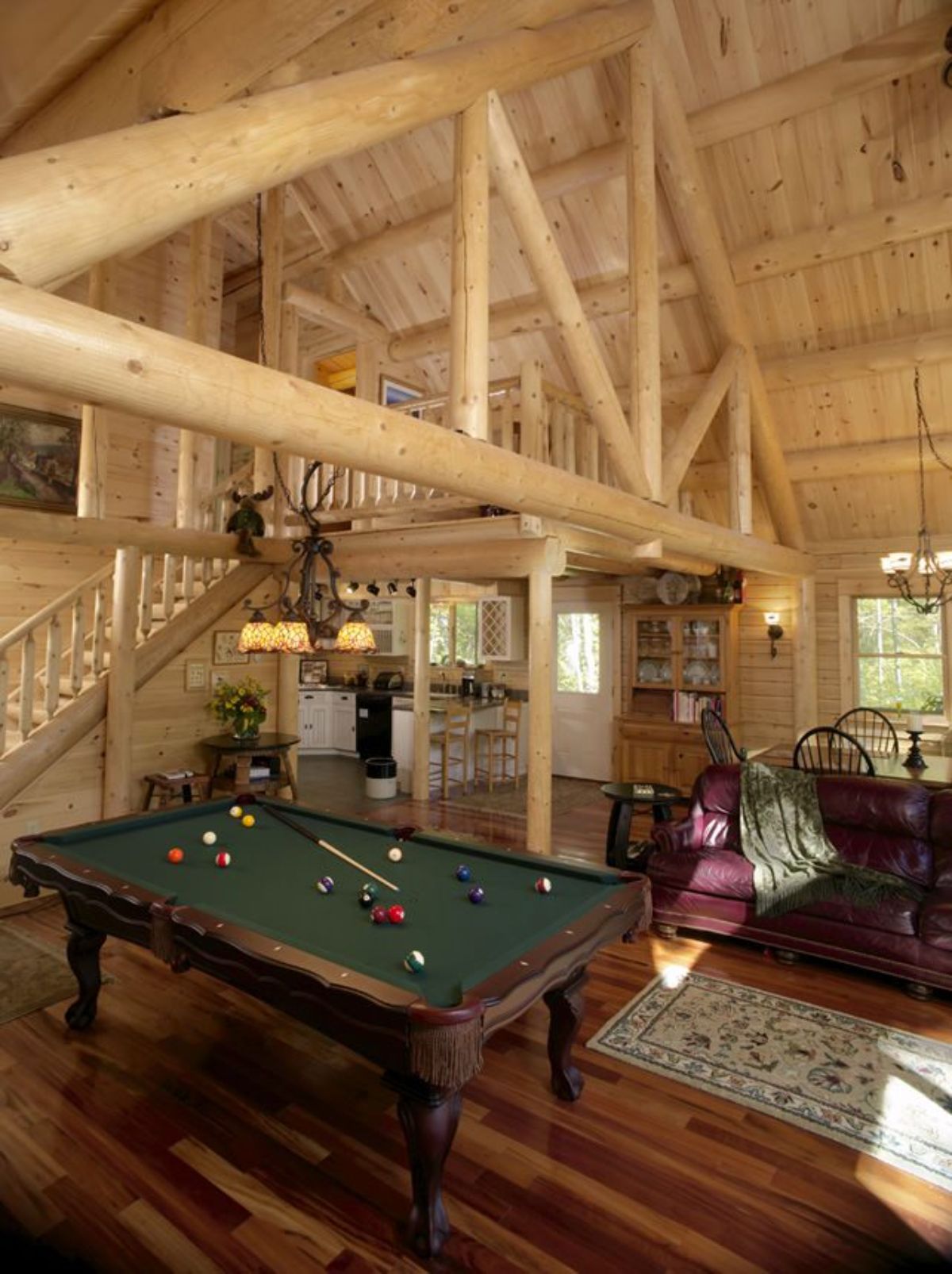 view of stairs behind green felt topped pool table by red sofas