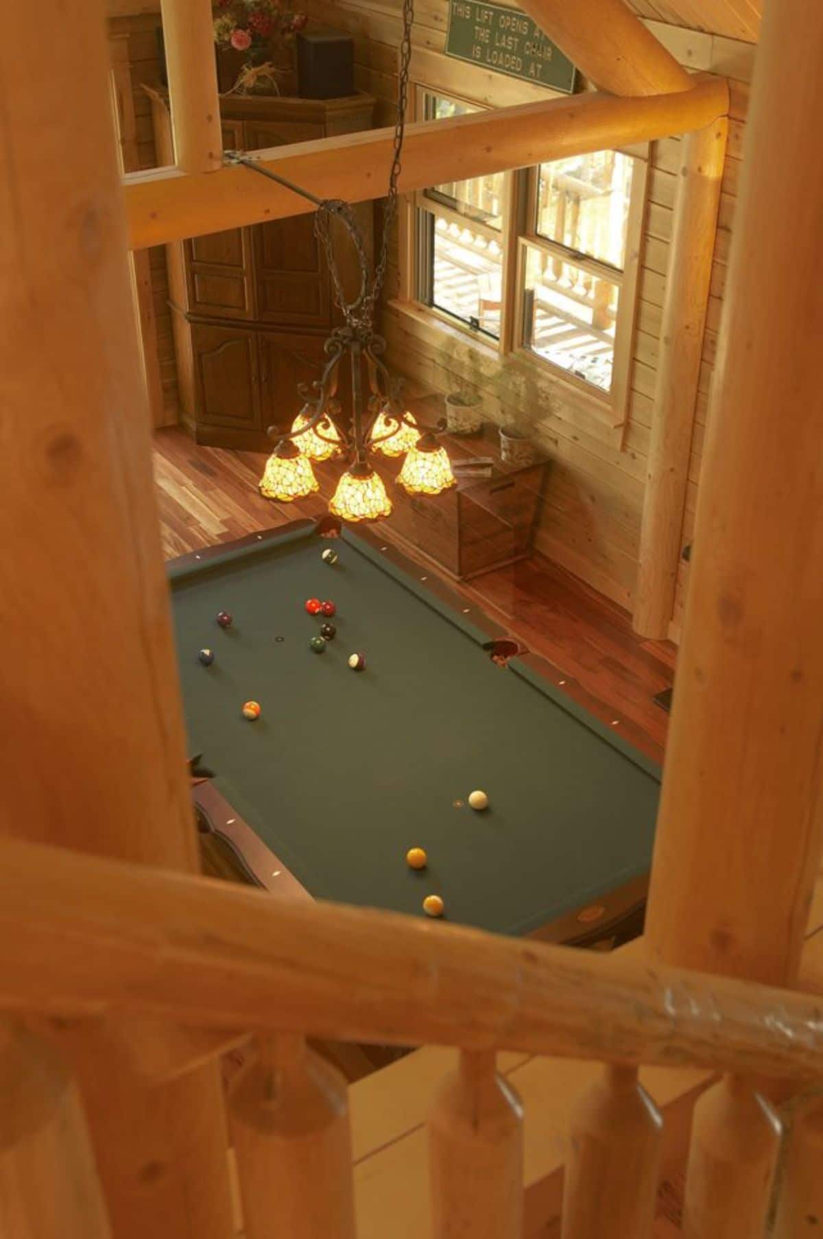 view from stairs down to green pool table in living room