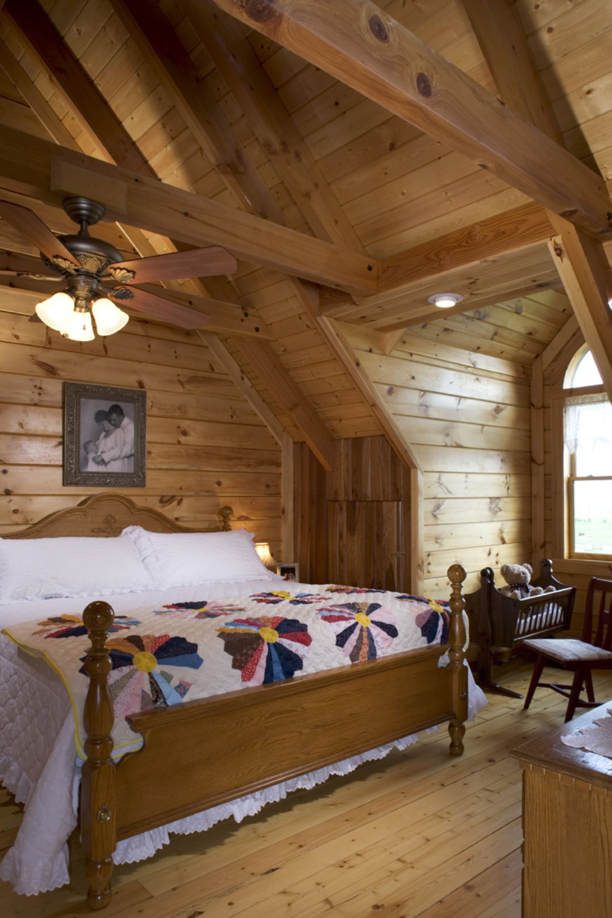 white linens with quilt on light wood bedframe in loft bedroom with dormer window to right