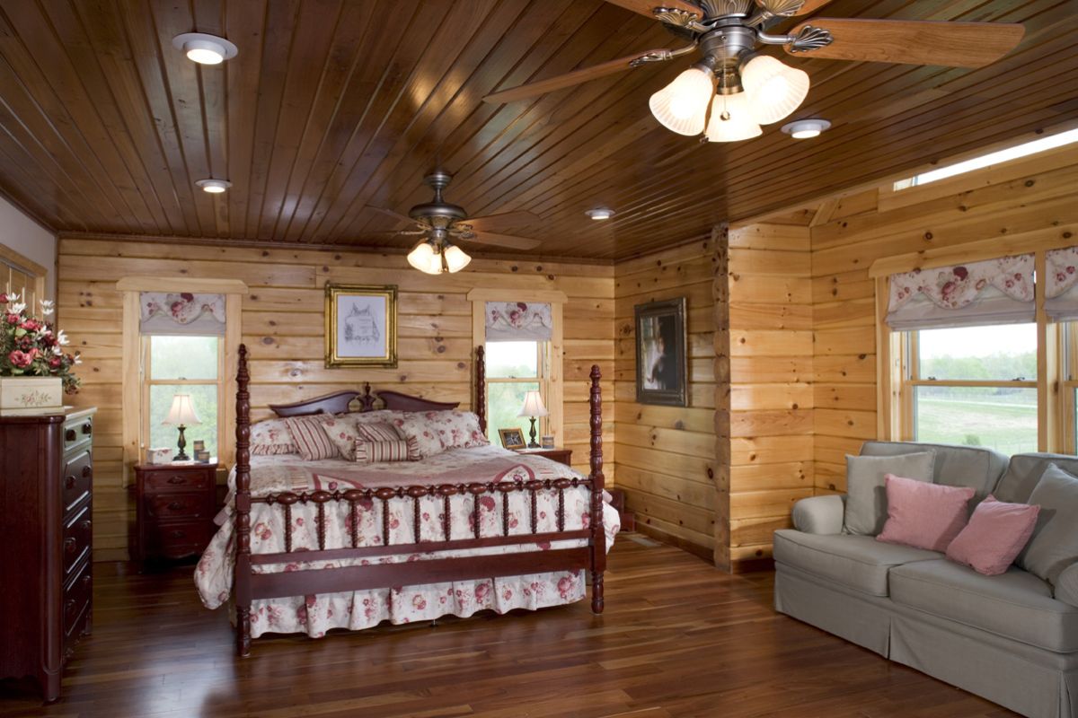 dark wood bedframe with white linens in log cabin bedroom with sofa on right