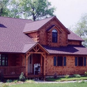 dark wood log cabin with dormer window above front entrance