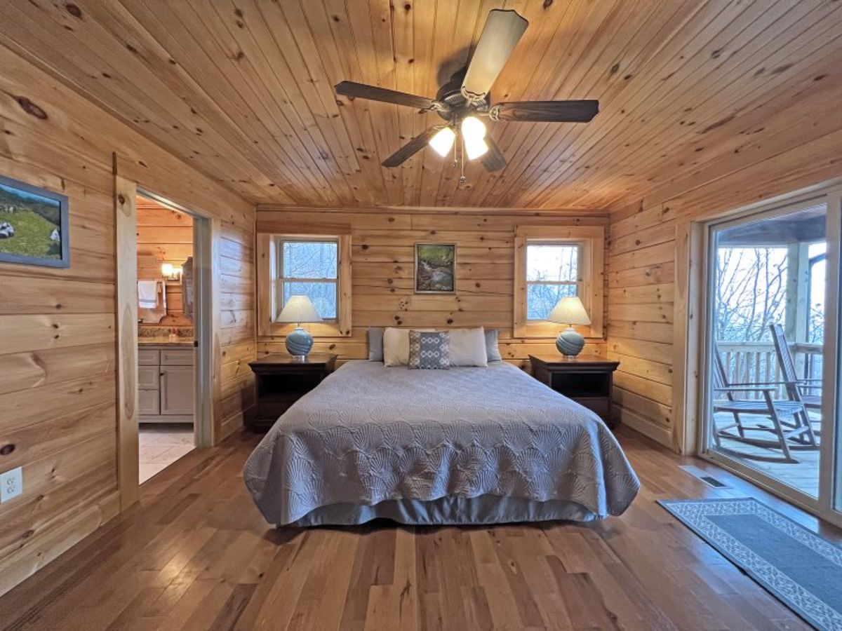 light grey bedding on bed beneath ceiling fan in log cabin bedroom