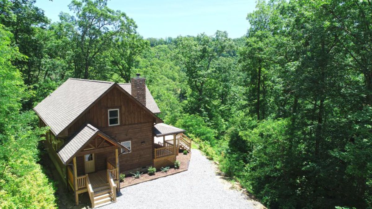 dark wood cabin with chimney on rigth side of light shingled roof