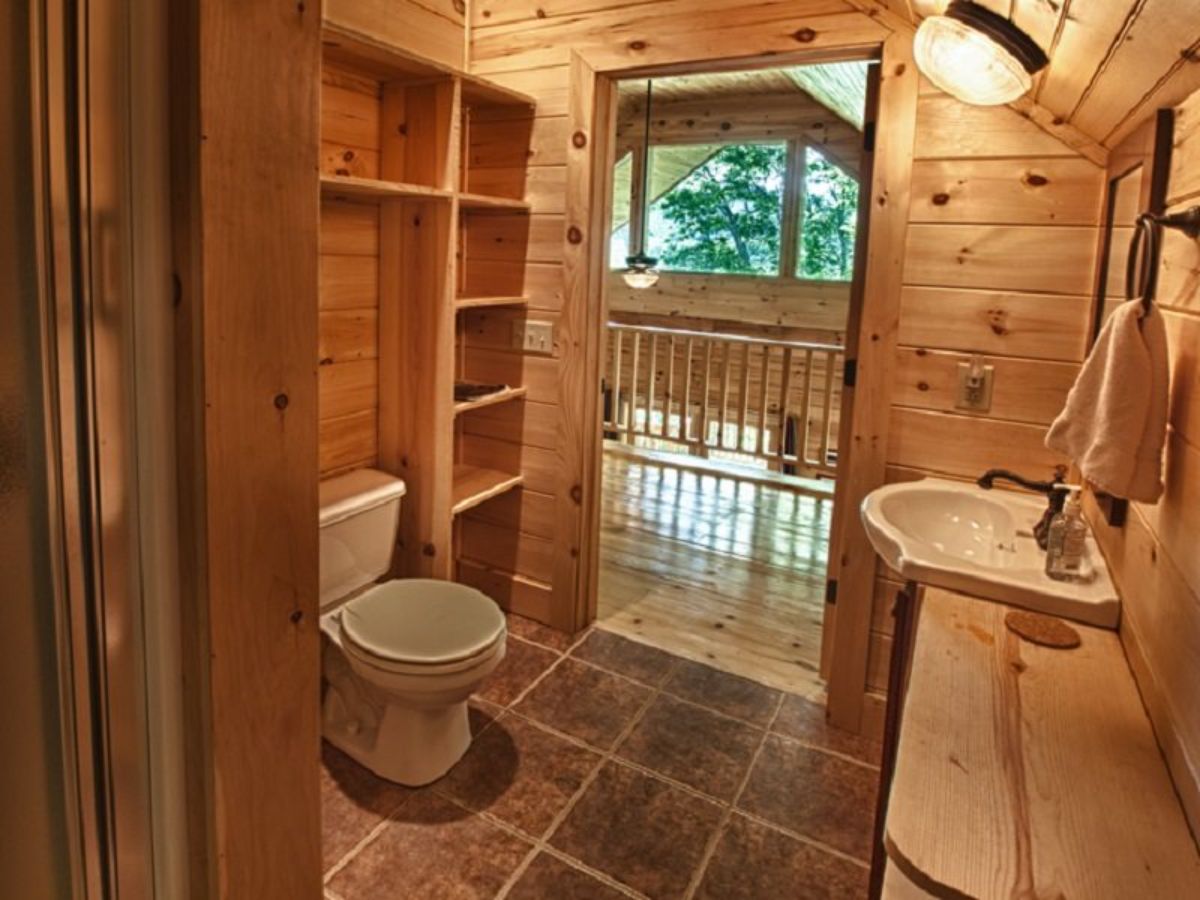 white toilet against left with open shelves and door to deck on back wall