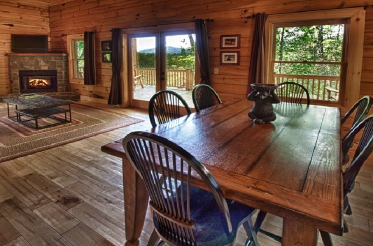 rounded edge wood chairs around dining table inside cabin with sliding glass doors in background
