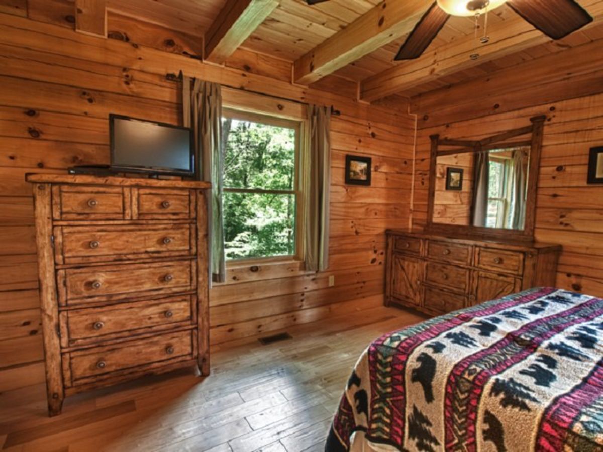 window next to chest of drawers holding small television with edge of bed in foregrund