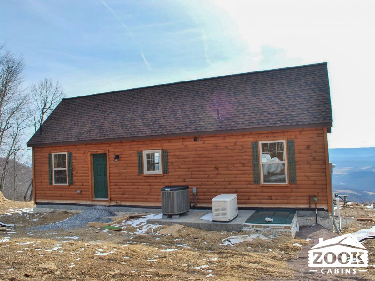 back of log cabin with three windows and green door overlooking valley