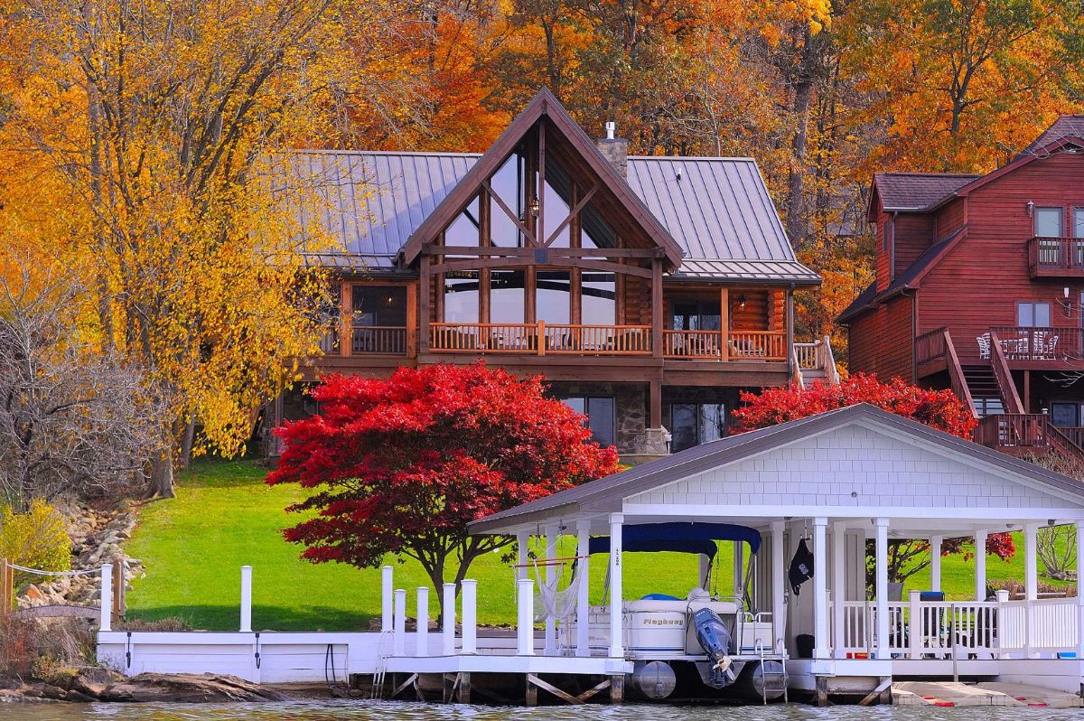 log cabin on hill behind boat dock and red trees