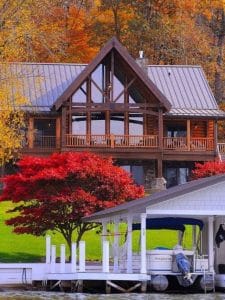 log cabin on hill behind boat dock and red trees