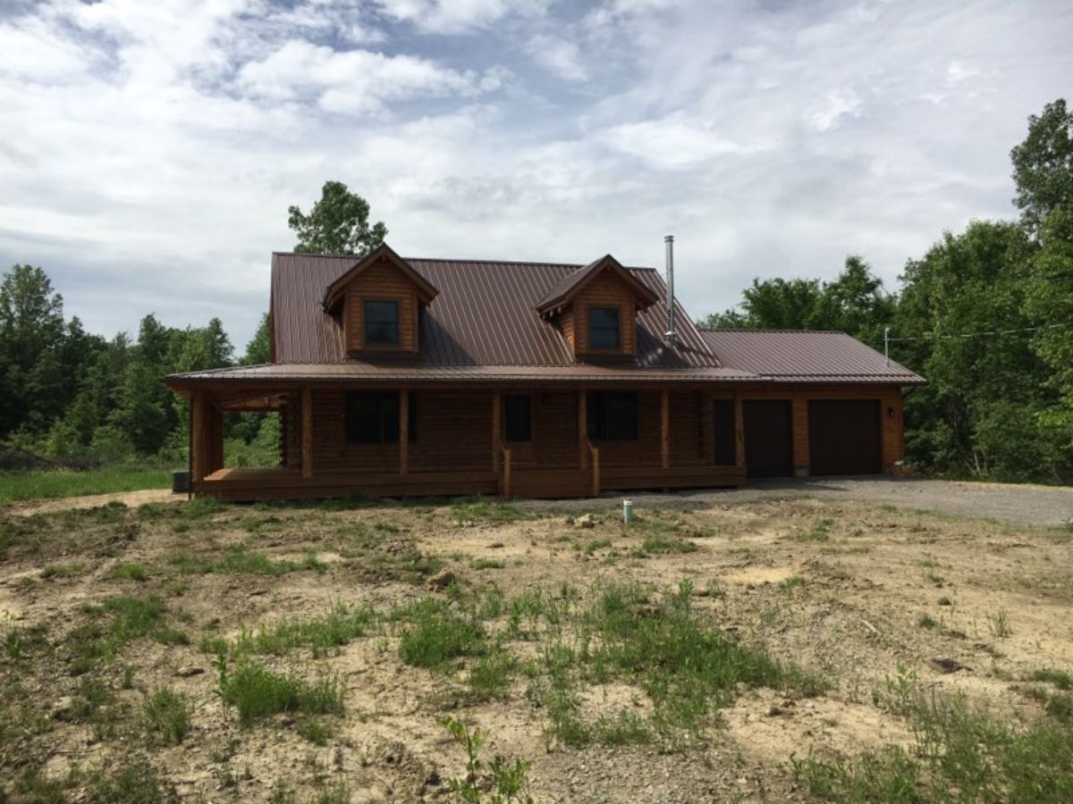 log cabin with wrap around porch on field of dirt and grass