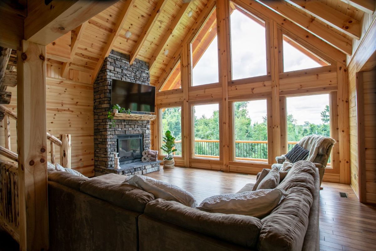 brown sofa in living room with wall of windows and stone fireplace in corner