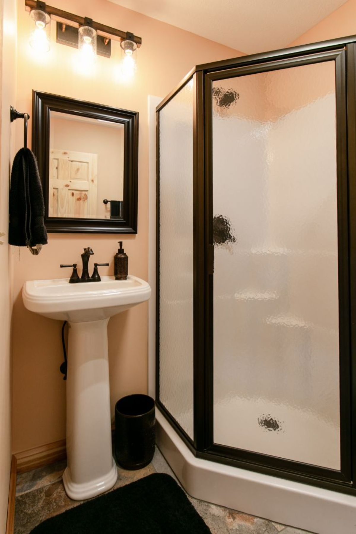 bathroom with white pedestal sink under black trimmed mirror with black trim shower door on right