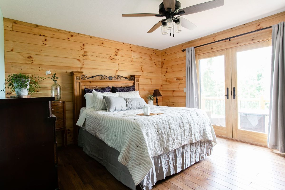 white bedding on bedframe against log cabin wall with glass doors on the right