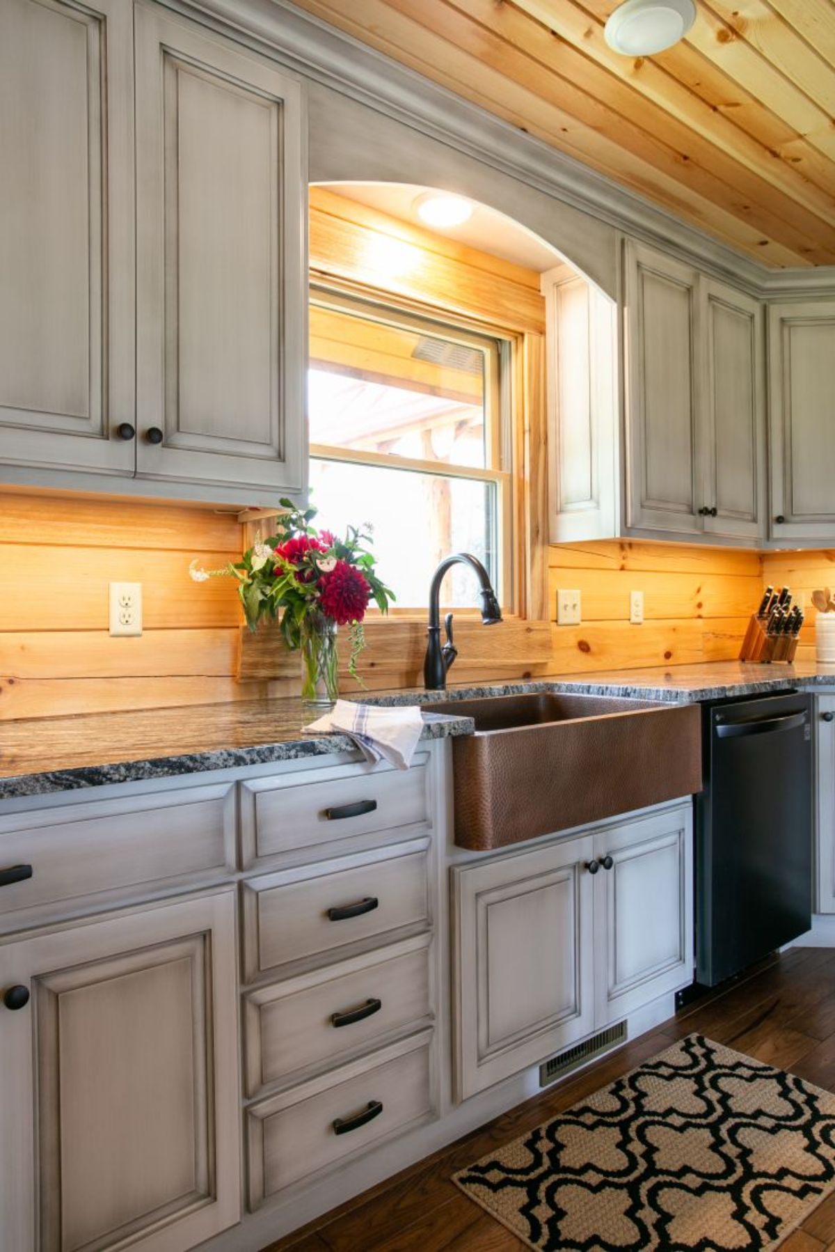white cabinets with bronze farmhouse sink under window and black appliances