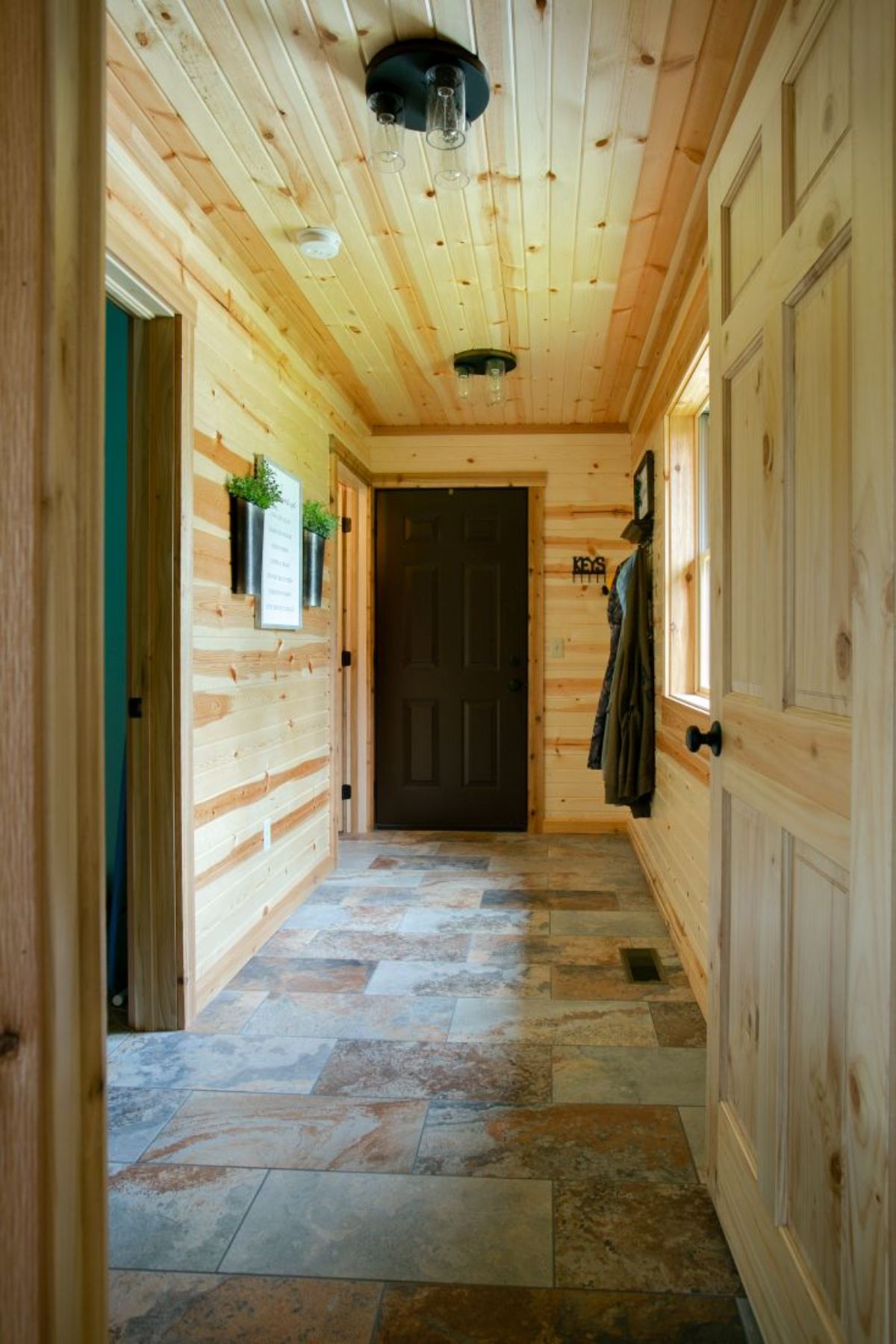light wood walls in hall of log cabin with dark brown door and tiled floor