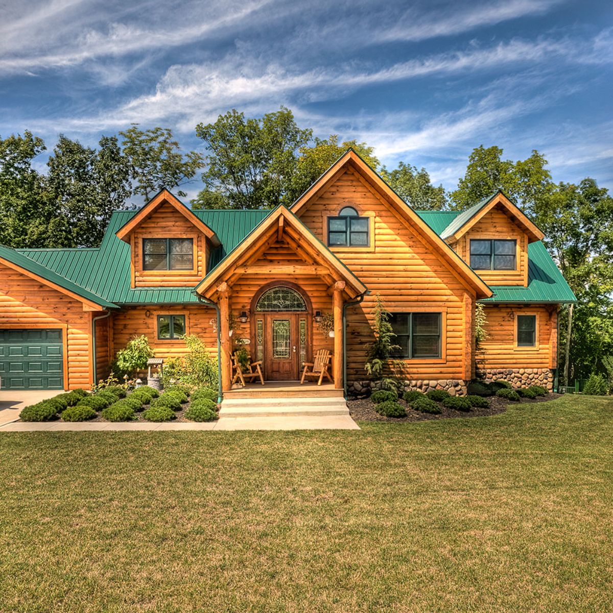 front of light wood log cabin and green roof with attached garage