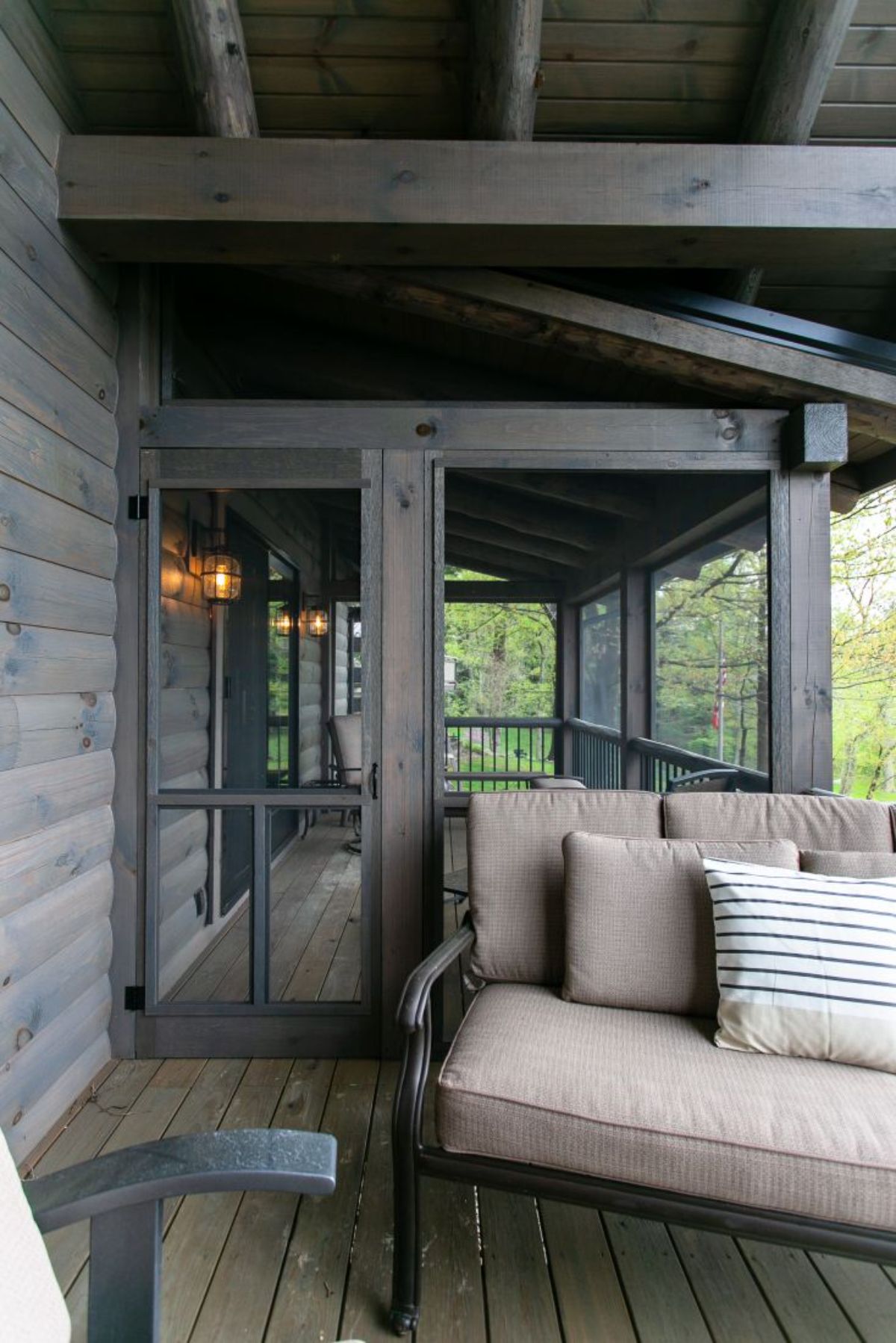 entrance to screened room of log cabin with gray wood walls and cream sofa outside door