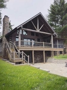 back of log cabin with staircase on left and covered porch above walkout basement