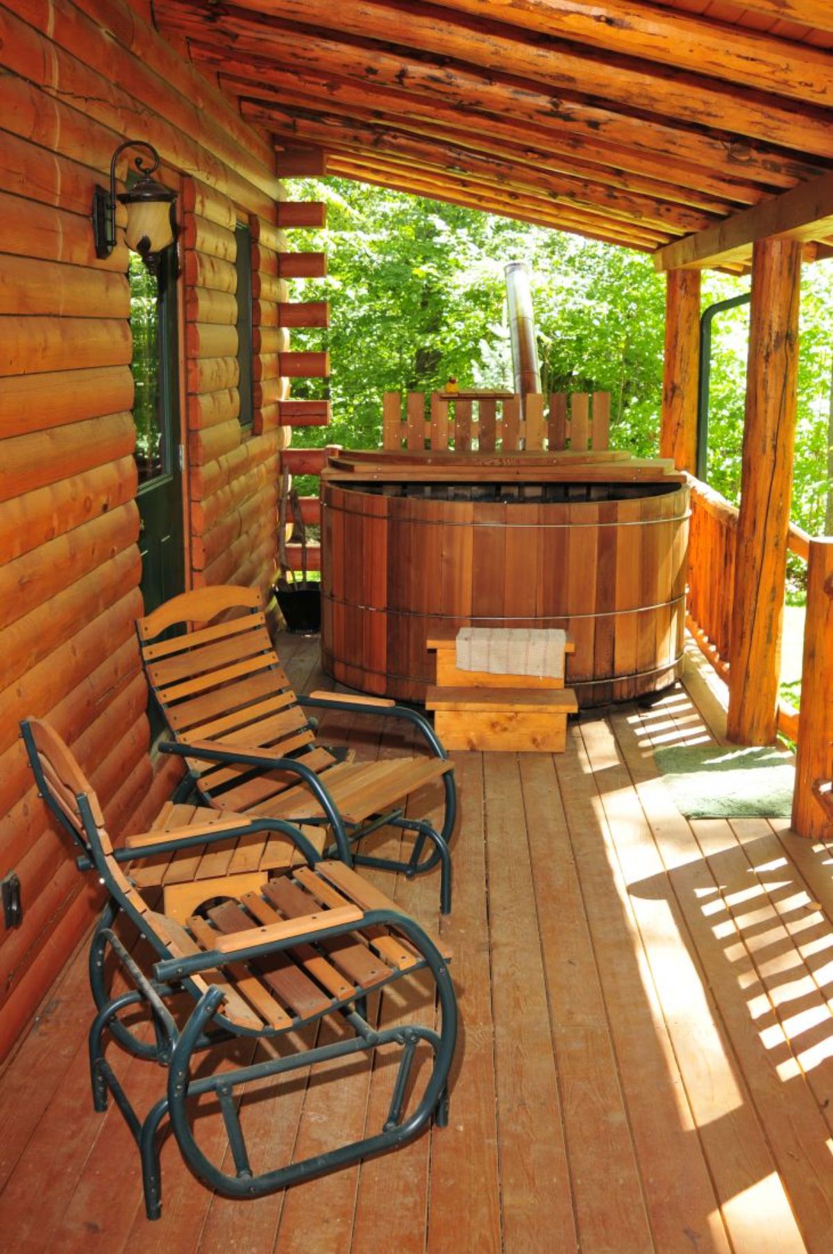 wood lined hot tub on end of covered porch of log cabin
