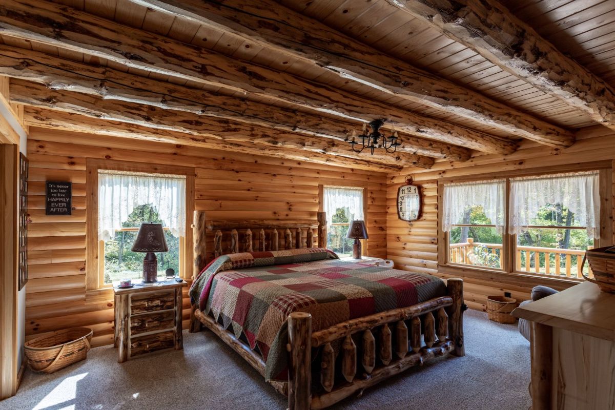 bed against wall between two windows with large window on right in log cabin