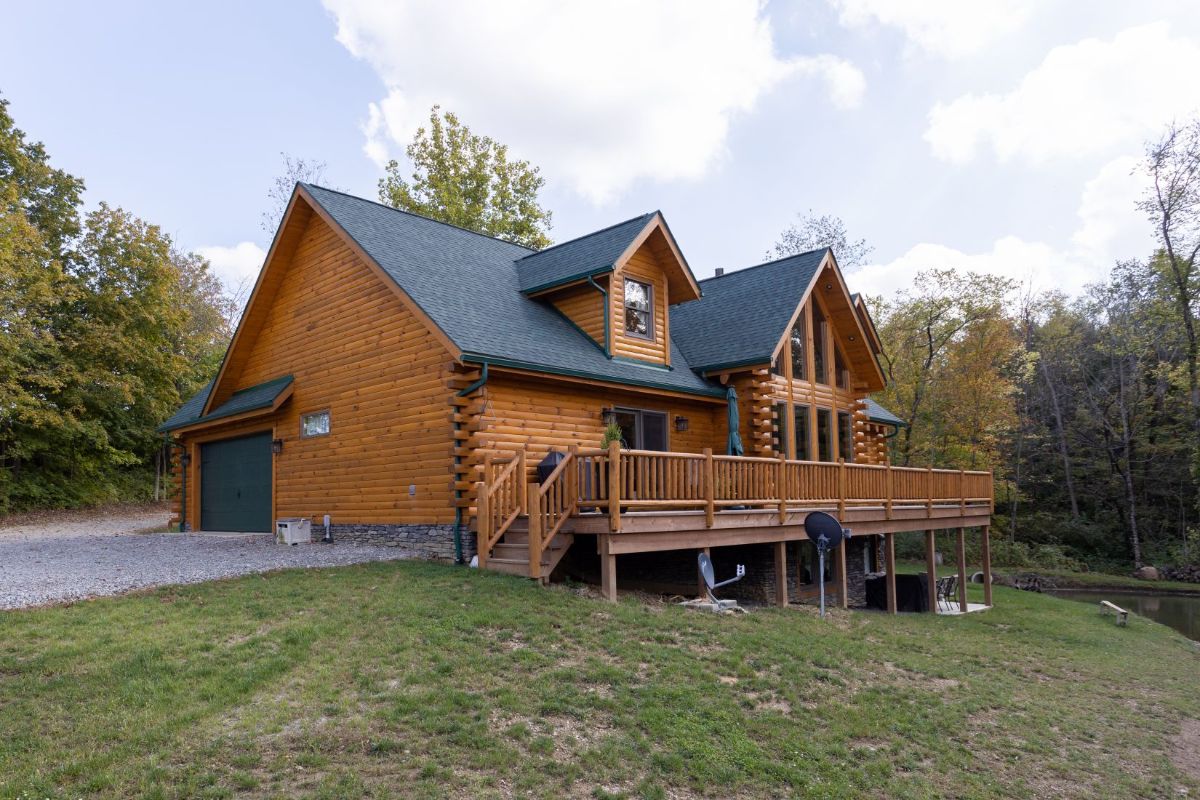 open deck on back of log cabin with driveway on left of image