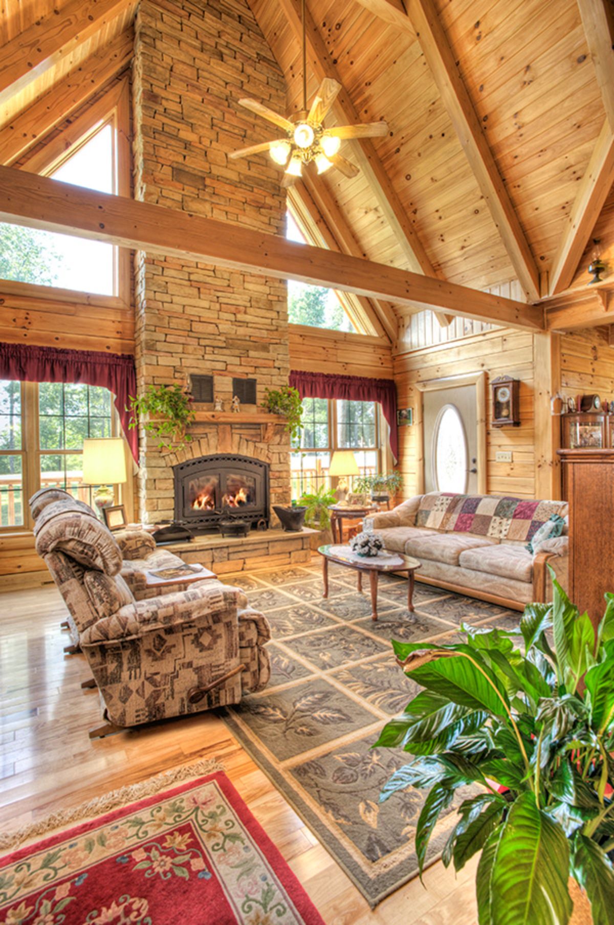 floral chair and sofa on rug in front of fireplace and wall of windows in log cabin