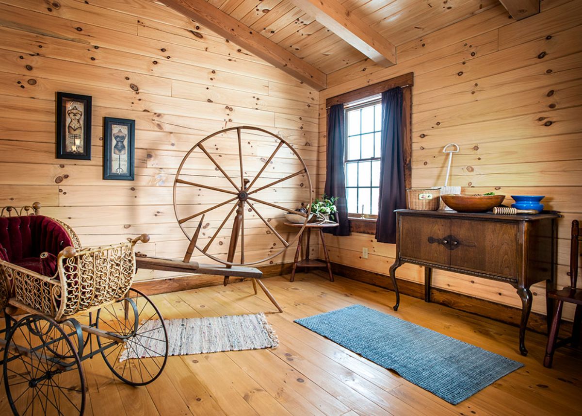 open room with spinning wheel against log wall near window