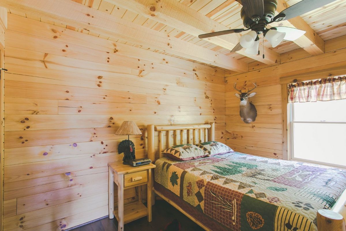 ceiling fan above bed with log bedframe and log walls