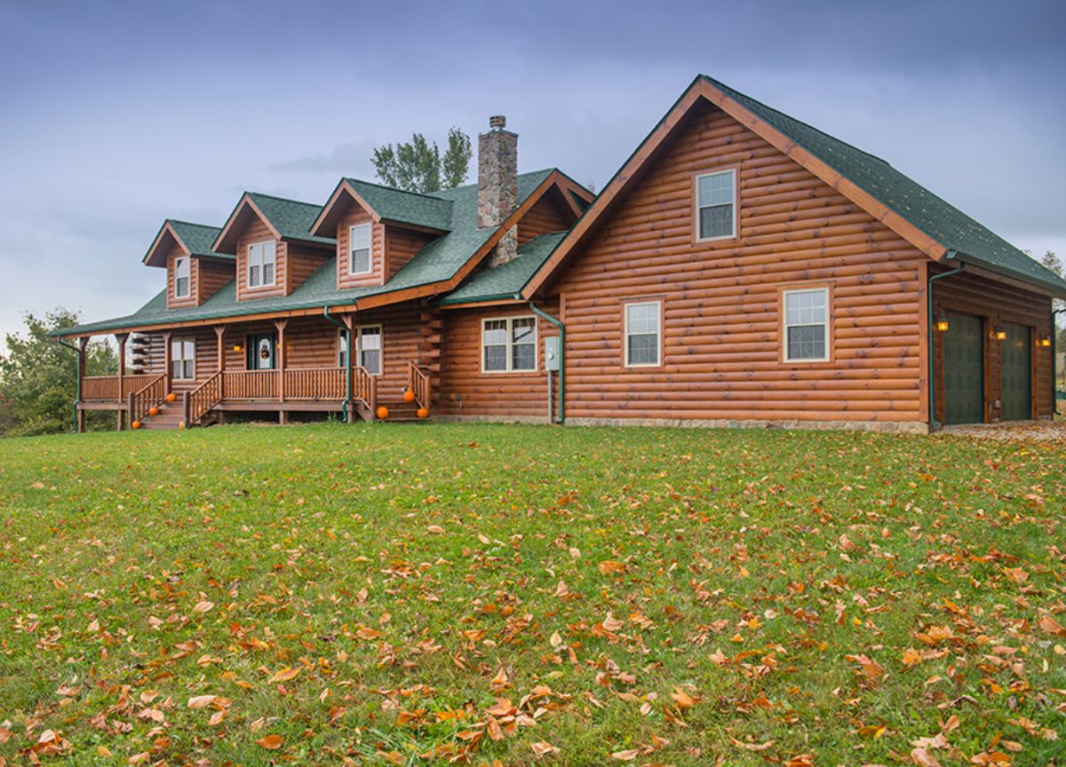 log cabin with small covered porch and green roof on hill of grass