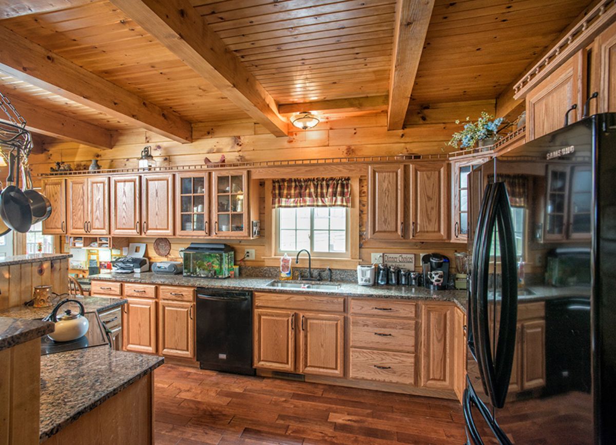 black refrigerator on right with medium stain wood cabinets against wall with window