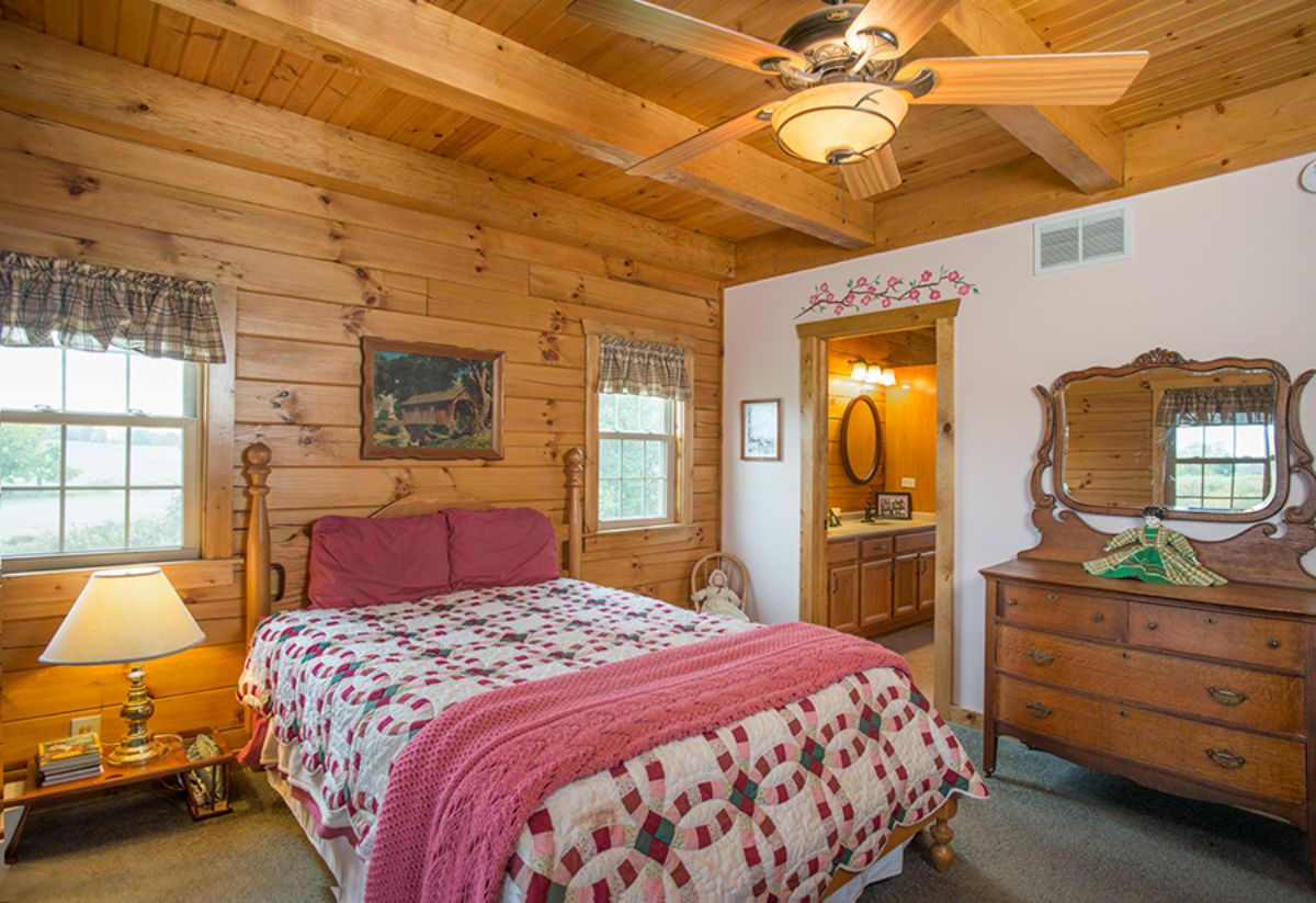 dark pink and white bedding on bed in log cabin bedroom showing bathroom through door on far right