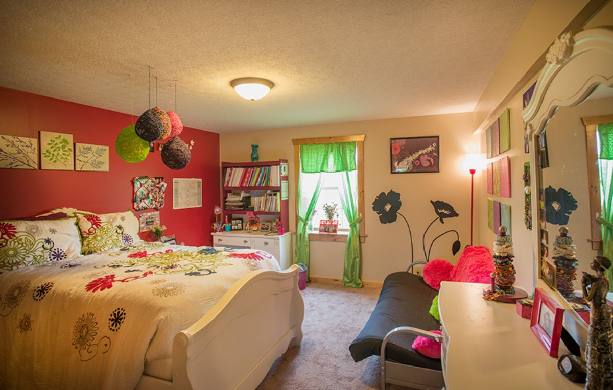 red wall on left of ids bedroom with green curtains and white bedframe