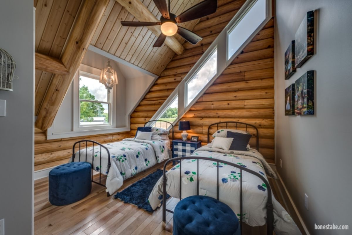 two twin beds with white and blue comforters in second floor bedroom with slanted windows on walls