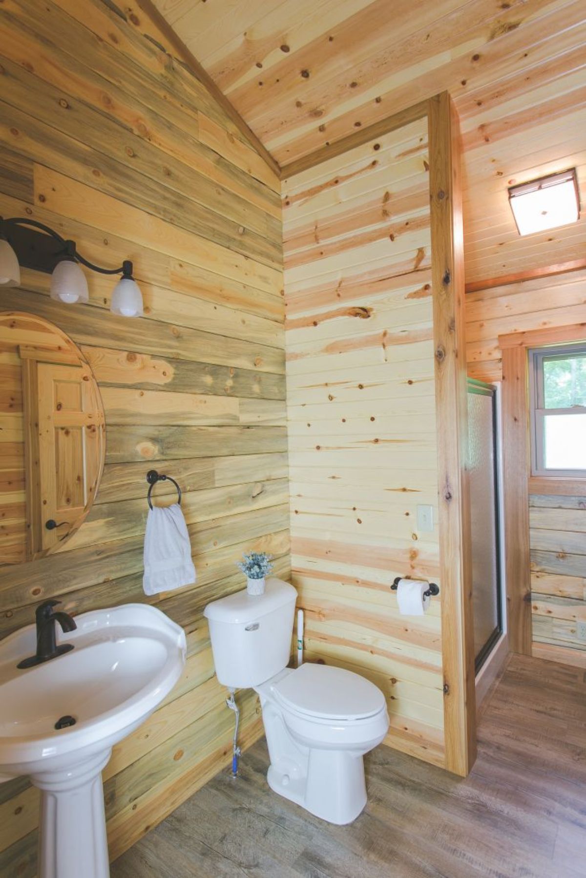 white pedastal sink next to white toilet in bathroom with wood walls