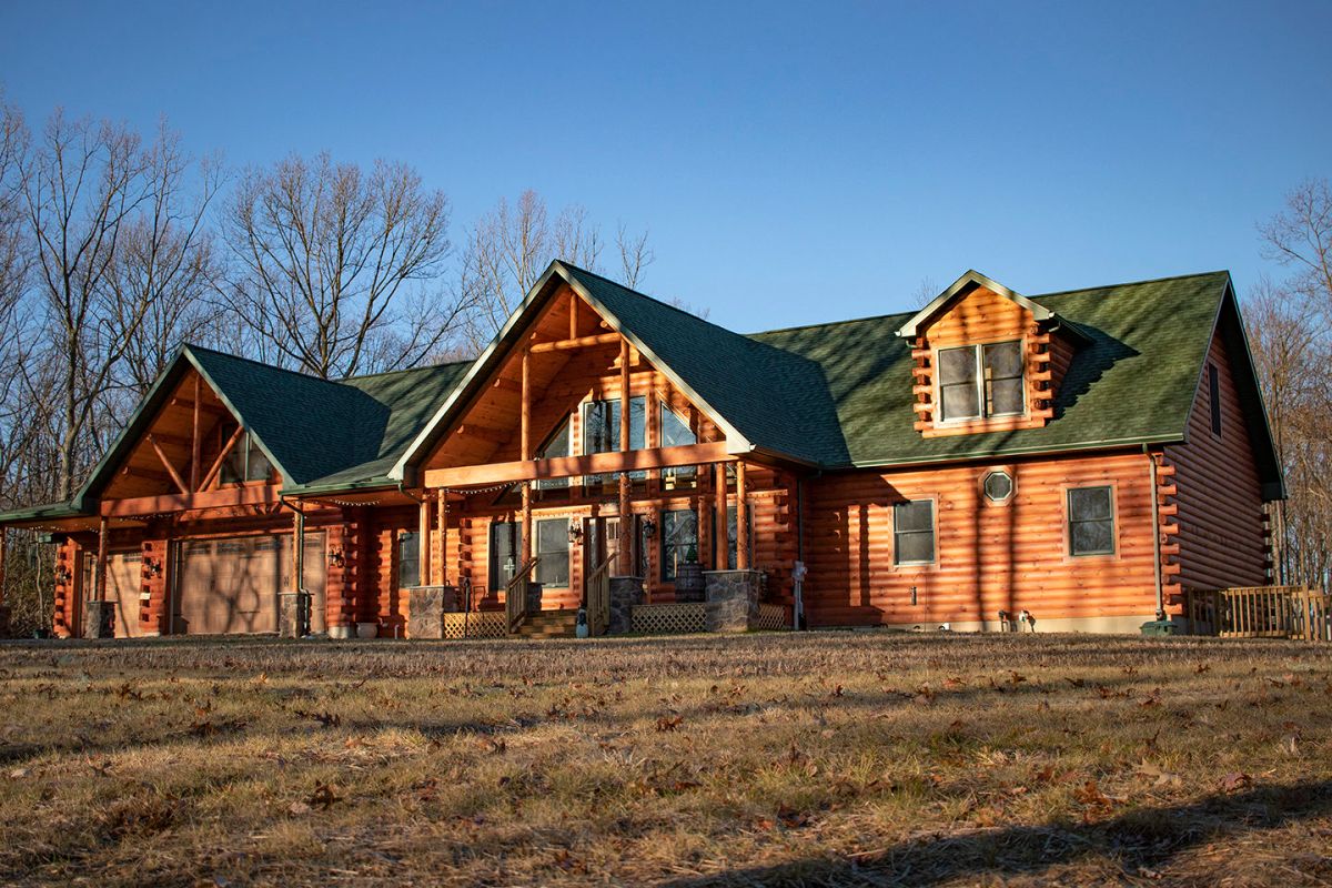 front of log home with green roof and covered porch