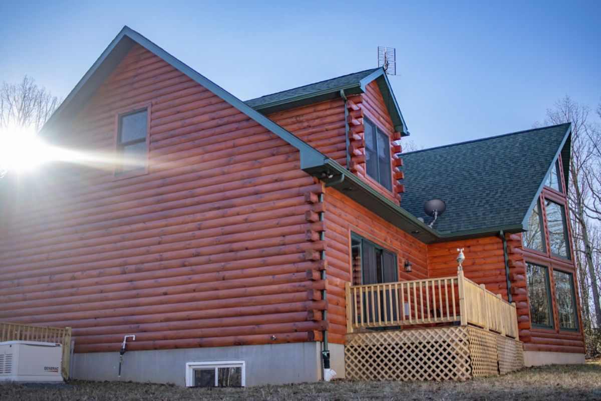 end o log cabin with medium red wood stained logs and light wood decking