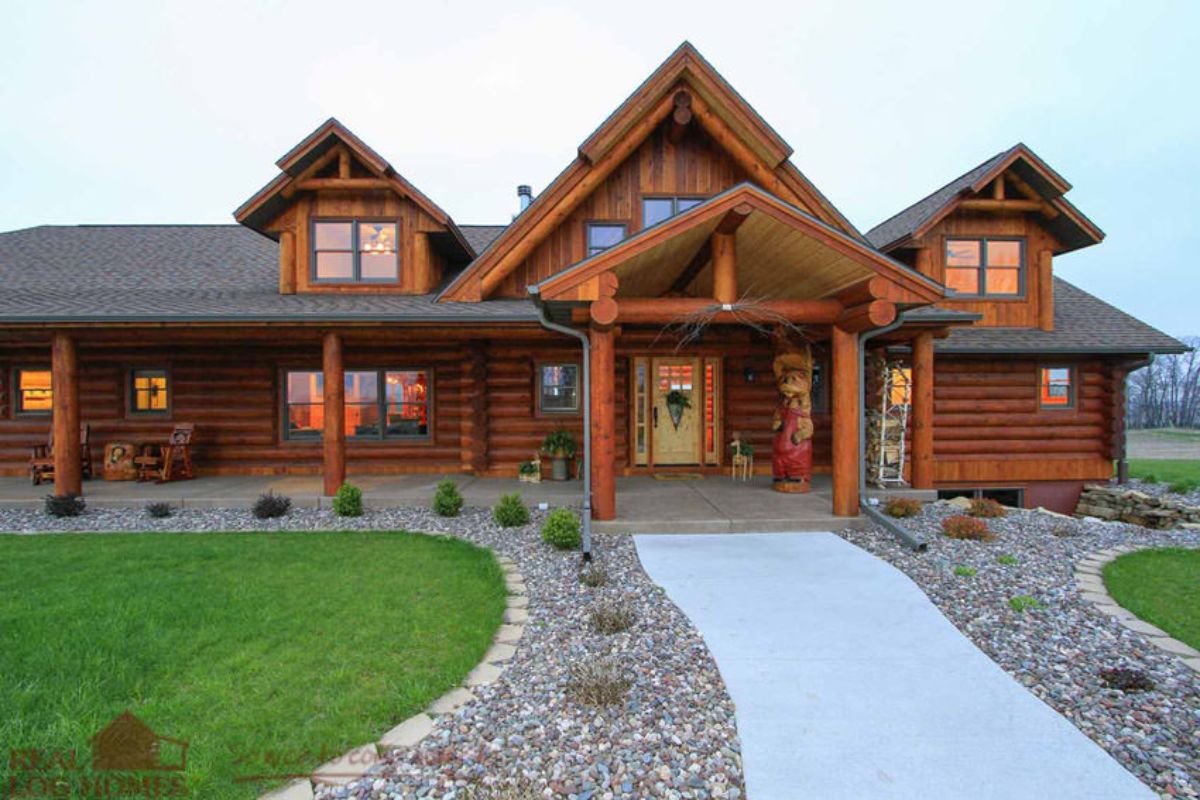 sidewalk to front of log cabin with gravel and shrubs on both sides