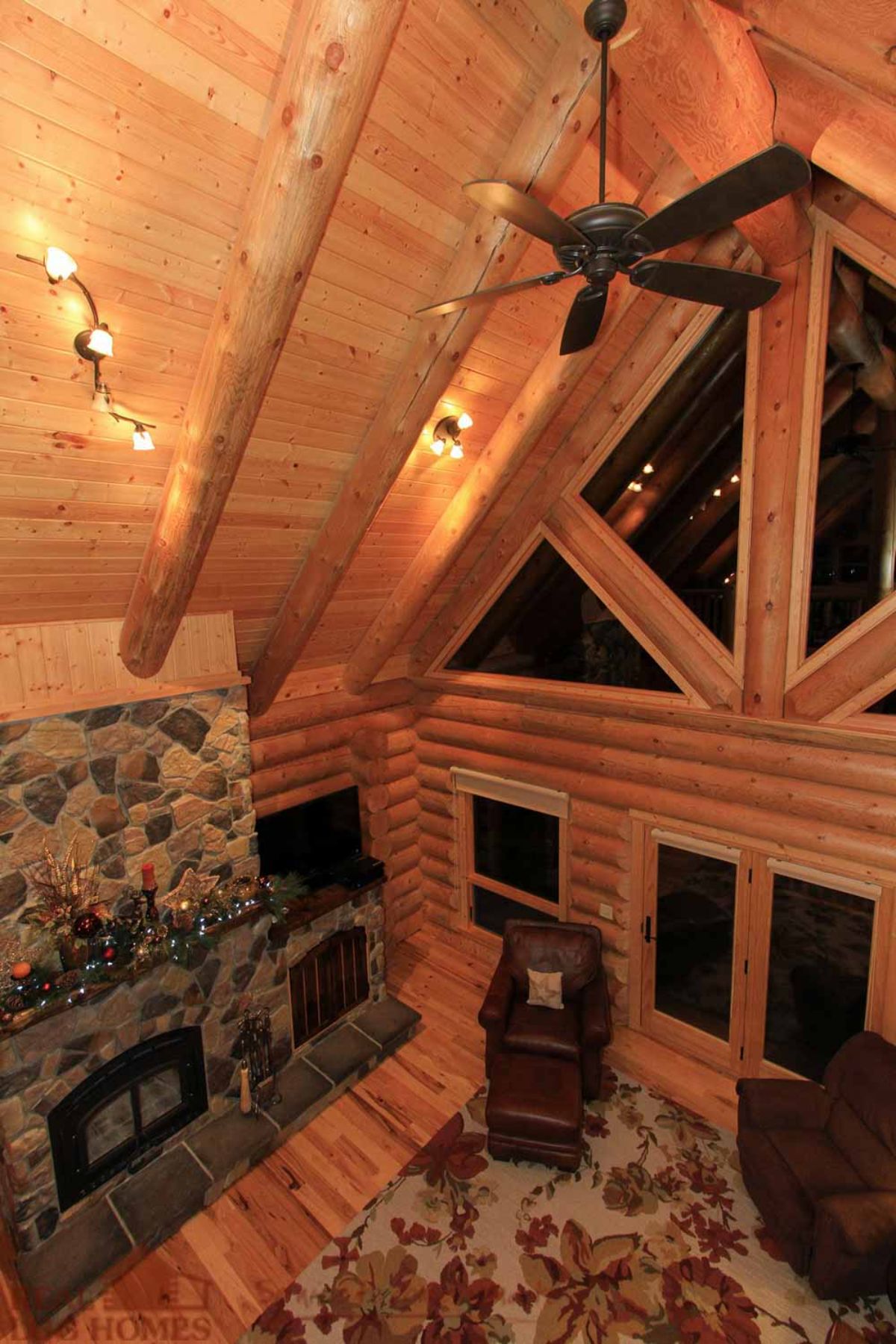 view from loft landing into main floor of log cabin with stone fireplace on left