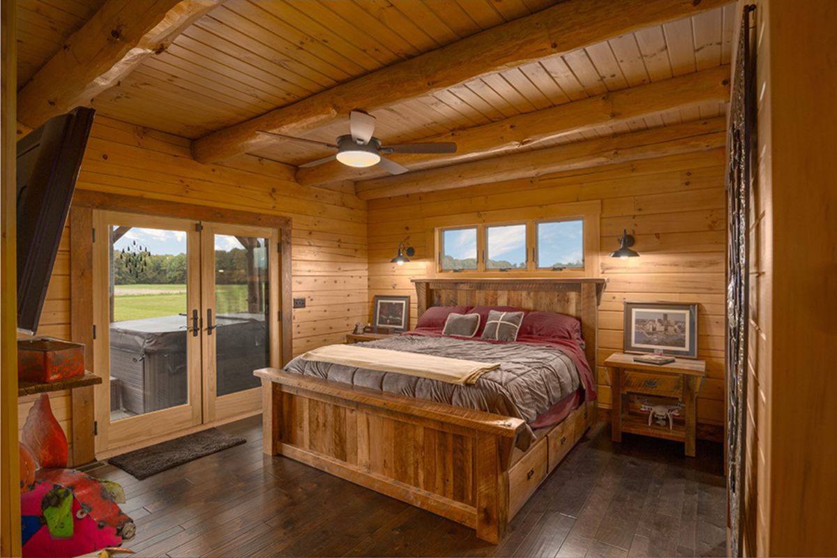 wood bedframe against wall of windows with doors to patio on left