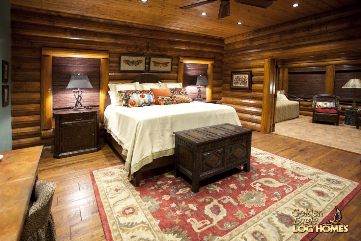 black chest at end of bed with white bedding sitting against log wall with paisley rug