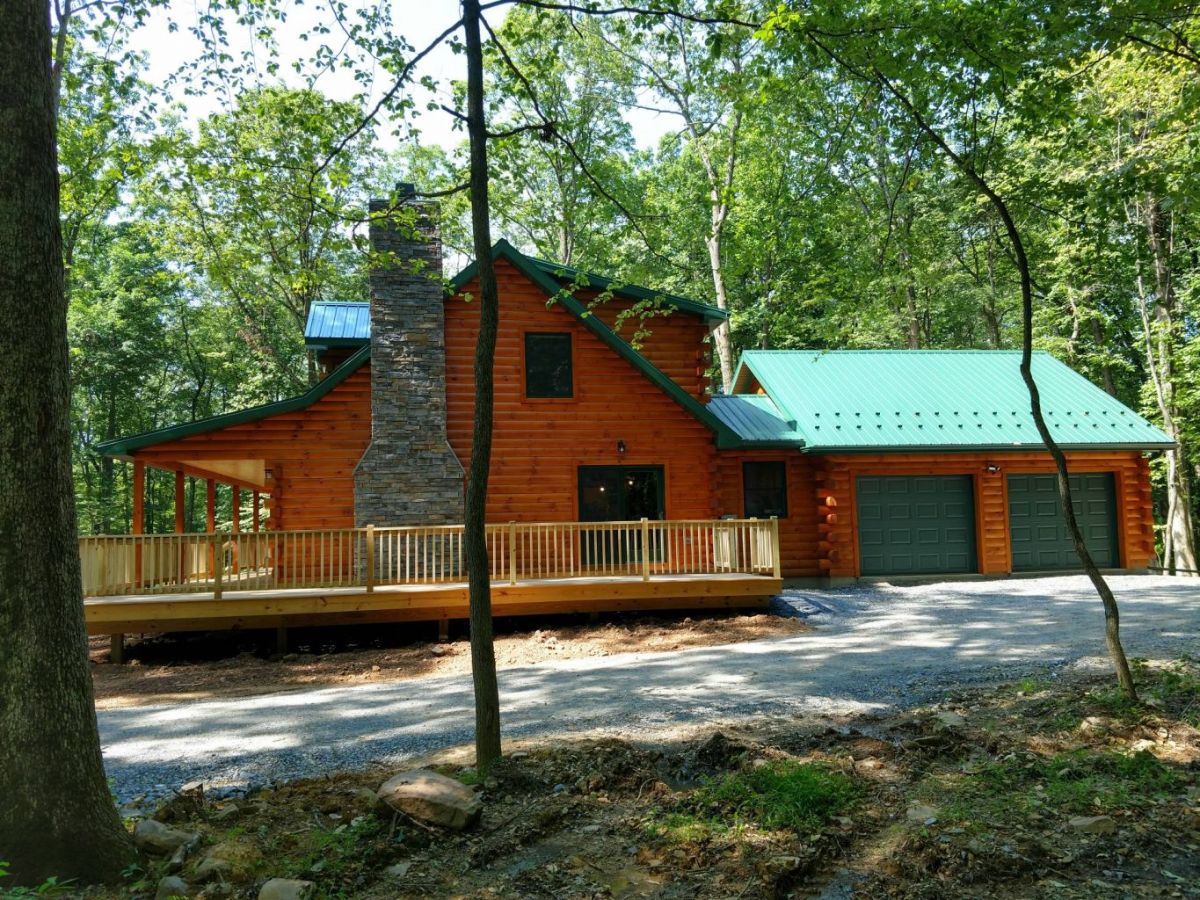 side of log cabin with green garage doors and open porch by chimney