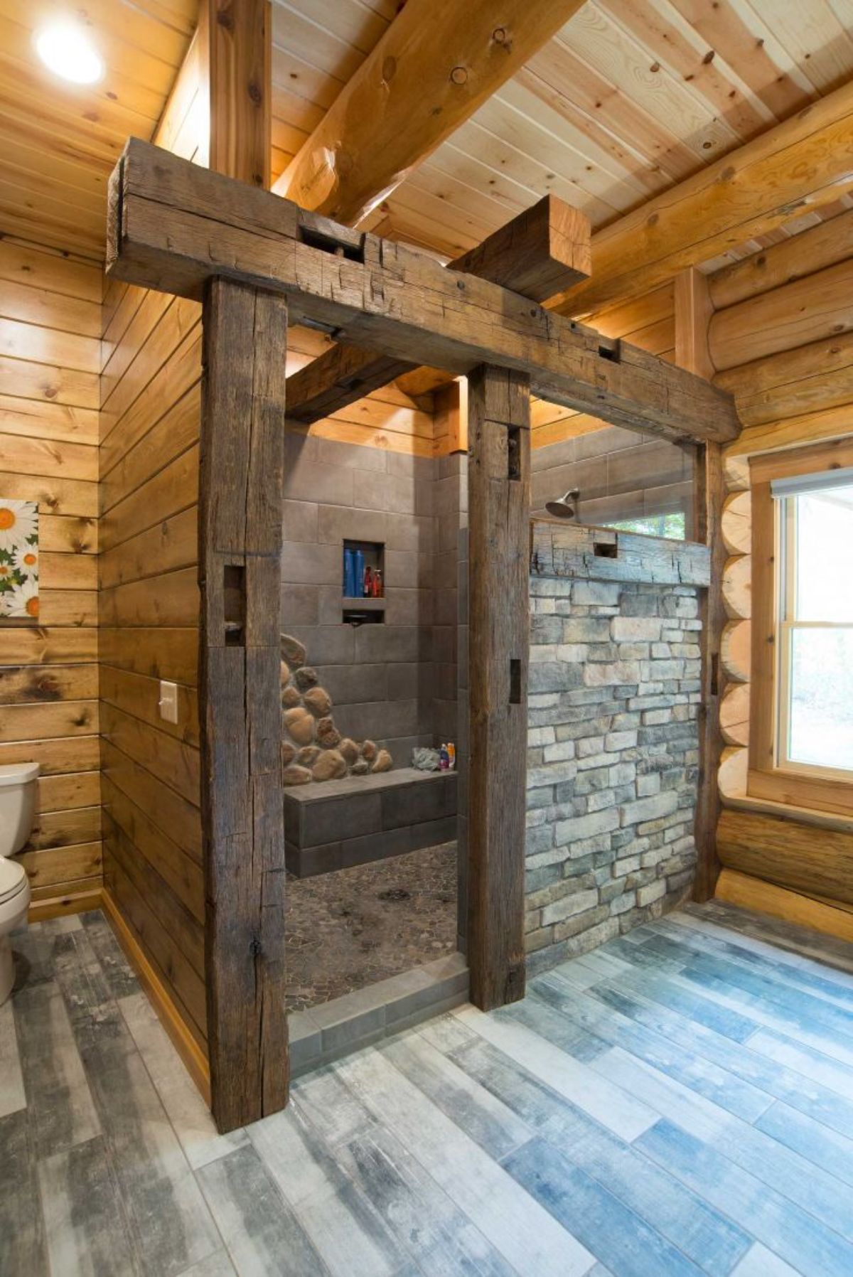 tiled and stone lined shower in log cabin bathroom with window beside shower
