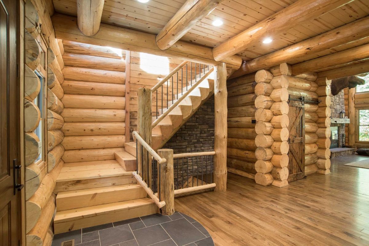 stairs against stone wall leading to log cabin second floor with round log walls